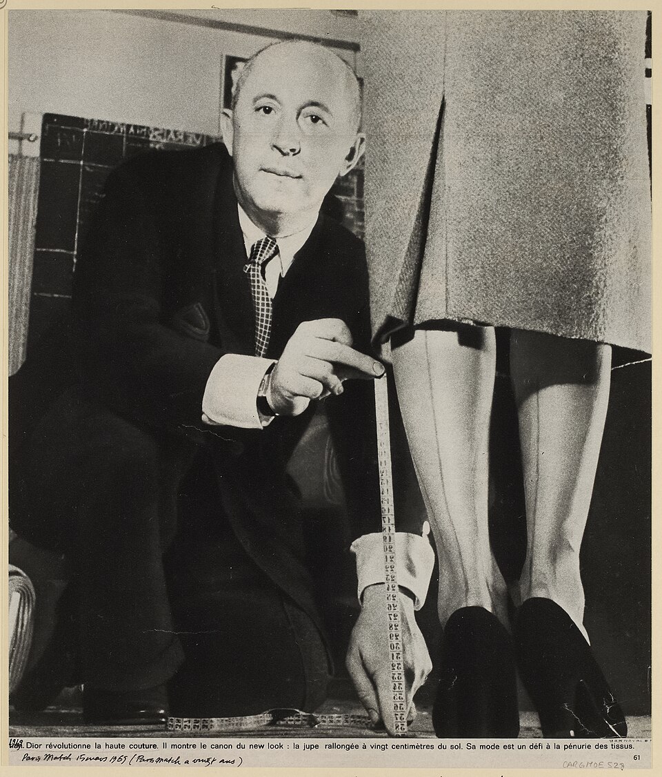 Christian Dior crouching with a tape measure to check a model's hemline.